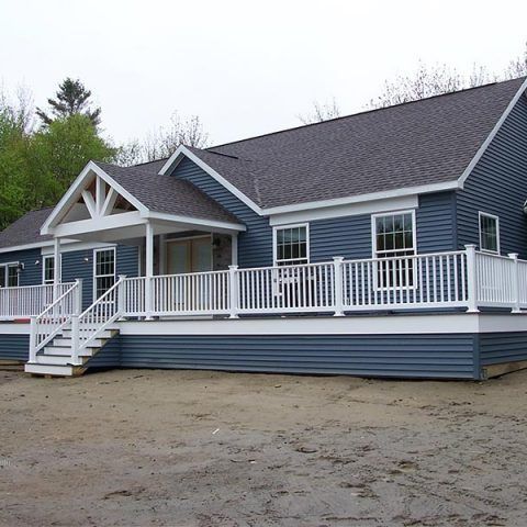 Blue house with white porch and railings on a gravel lot