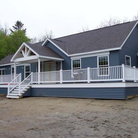 Blue house with white trim, front porch, and accessible ramp on a sandy lot.
