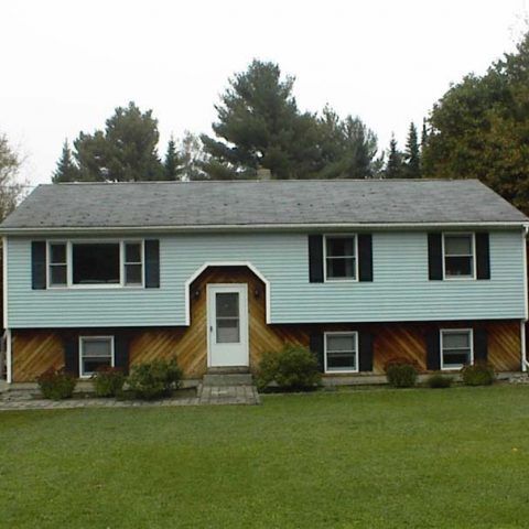 Light blue split-level house with white trim, central doorway, and a green lawn in front