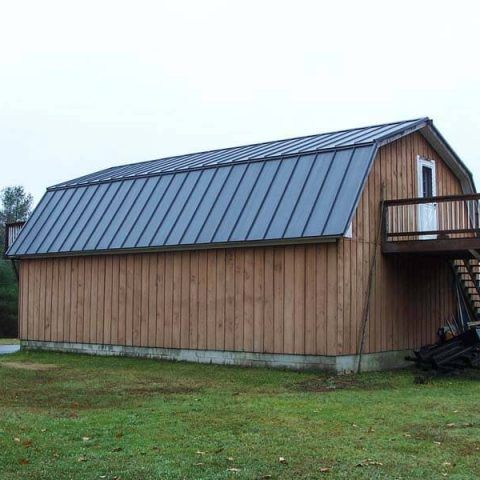 Wooden barn with a gray metal roof and small balcony on a grassy field