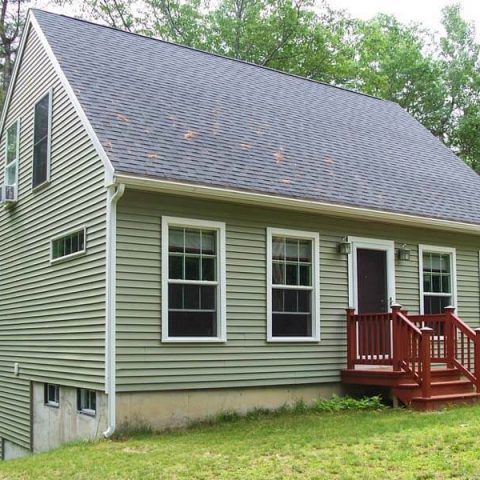 Small green house with white-trim windows, dark roof, and a red front porch in a grassy yard.