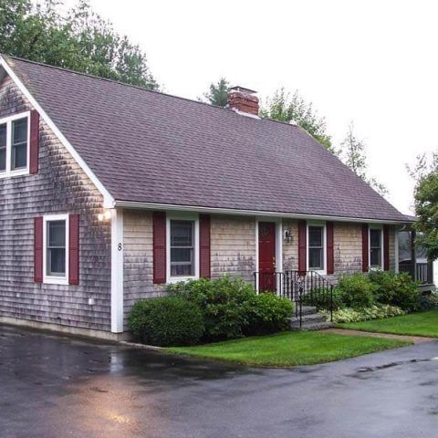White house with red shutters, steep roof, and a wet driveway on a rainy day