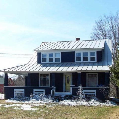 Snow-dusted farmhouse with a metal roof and yellow front door under a clear winter sky