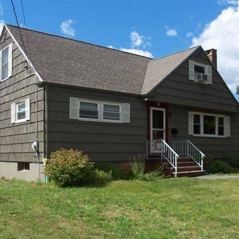Gray house with white trim and front steps on a grassy lawn under a blue sky