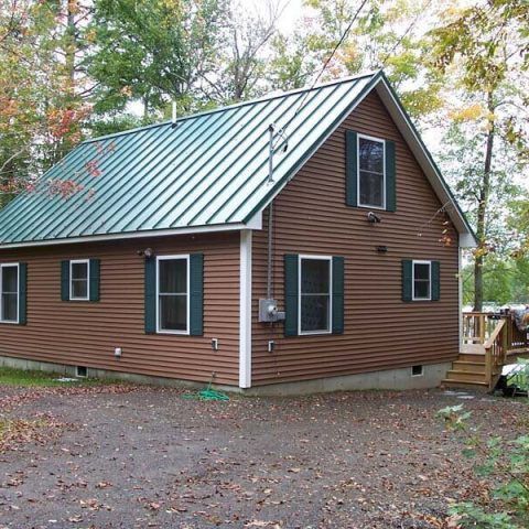 Brown cabin with green metal roof and dark shutters in a wooded yard