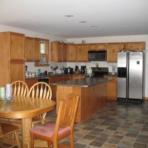 Wooden kitchen with cabinets, stainless steel fridge, tiled floor, and a round dining table with chairs
