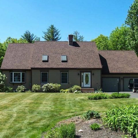 Single-story brown house with a large lawn, garage, and flower beds under a bright blue sky