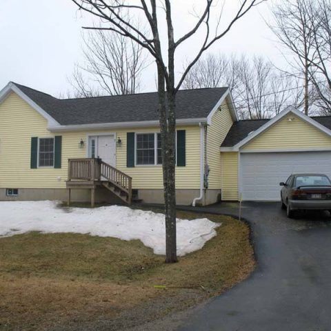 Yellow house with white garage, snowy yard, and a car parked in the driveway