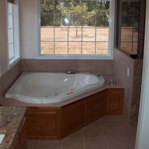 Corner bathtub in a tiled bathroom with large window and wood paneling