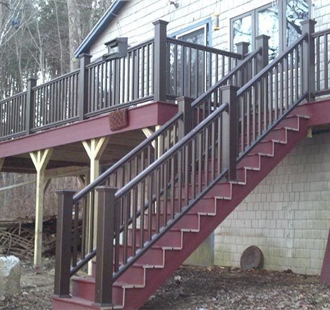 Stairway with dark railings leading to a raised wooden deck beside a house