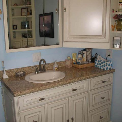 Bathroom vanity with white cabinets, granite countertop, sink, mirror, and toiletries against light blue walls
