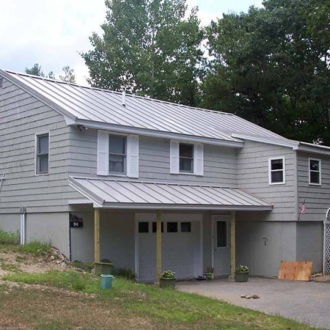 Gray two-story house with a metal roof, front porch, and trees in the yard