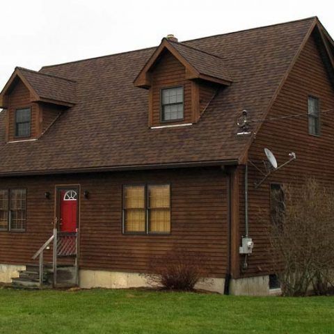 Red door on a brown house with dormer windows and a satellite dish on the side