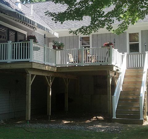 Raised wooden deck with white railing and stairs beside a house under tree shade