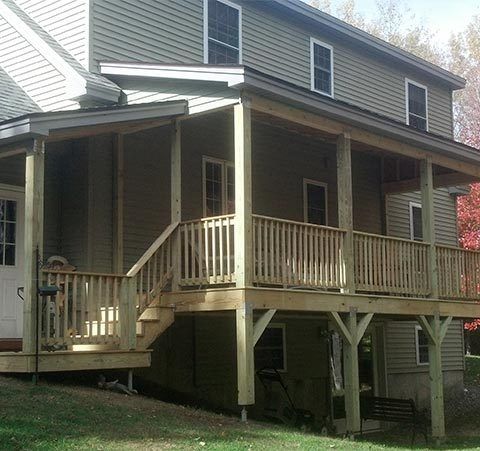 Two-story house with a covered wooden porch, railings, and steps on a grassy yard.