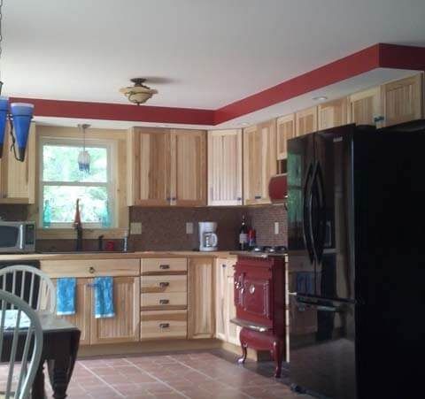 Kitchen with light wood cabinets, red stove, black fridge, and a window over the sink.