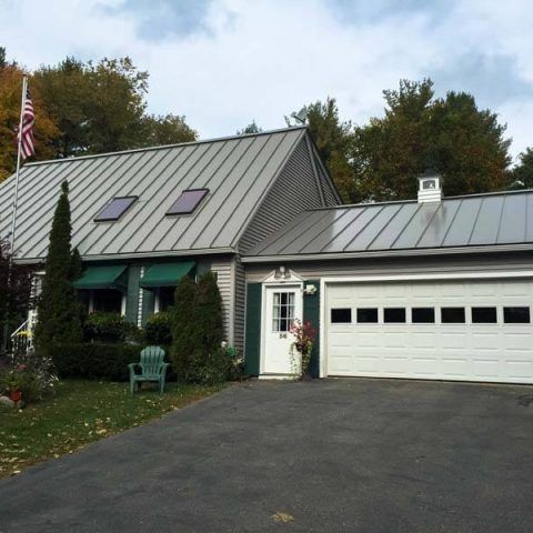 Suburban home with gray metal roof, white garage, and driveway surrounded by trees