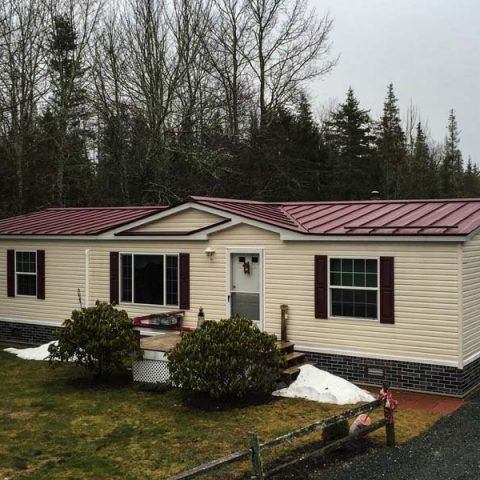 Single-story beige house with red metal roof and dark shutters on a cloudy day