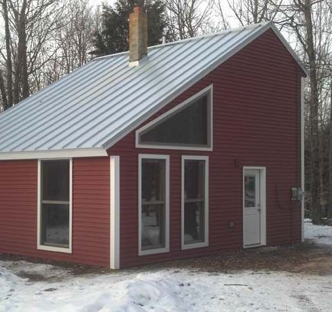 Red house with a silver metal roof and large windows in a snowy yard