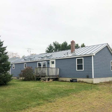 Blue single-story house with white trim, small porch, and a grassy yard under an overcast sky