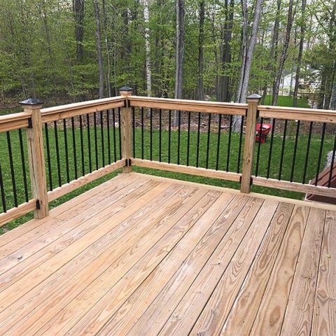 Wooden deck with black railing overlooking a green backyard and trees