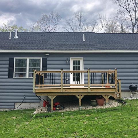 Gray house exterior with a small wooden deck and railing under a cloudy sky