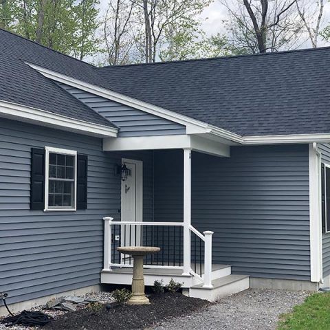 Blue-gray house exterior with small covered porch, white railings, and gravel walkway
