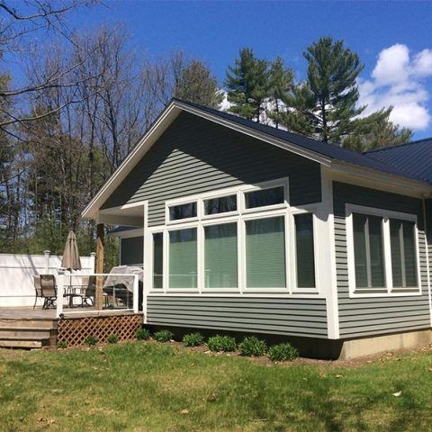 Gray house with large windows and a small deck in a sunny backyard.