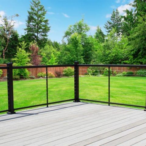 Wooden deck with black railing overlooking a lush green backyard and trees under a blue sky