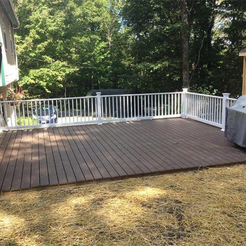 Wooden deck with white railing overlooking a wooded backyard on a sunny day