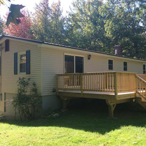 Single-story beige house with a wooden deck and stairs in a sunny backyard