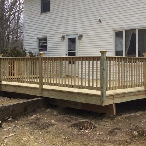 Raised wooden deck attached to a white house, with railings and stairs not yet installed.