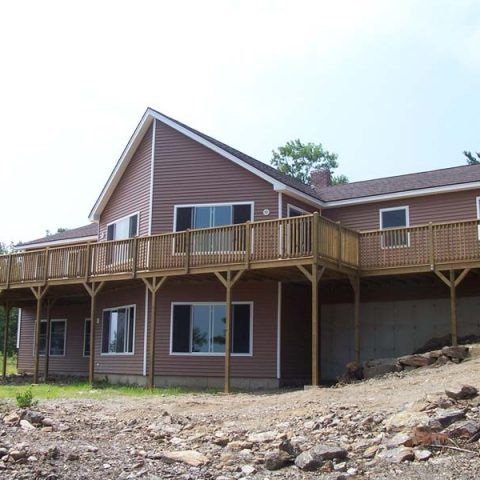 Large brown house with a wooden deck on a rocky hillside under a bright sky