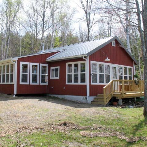 Red cabin with white trim and a small wooden porch in a wooded clearing