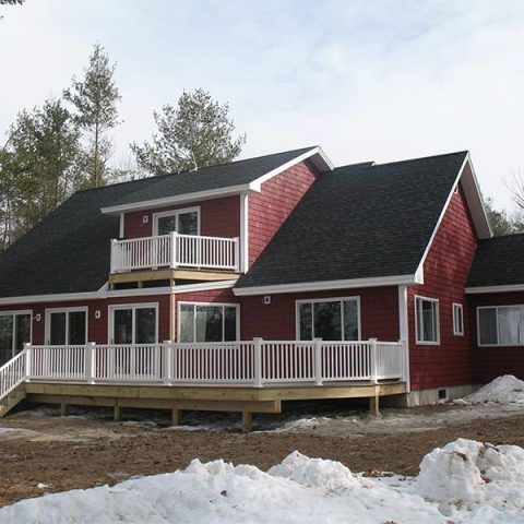 Red two-story house with white trim and porch, surrounded by snow and trees.
