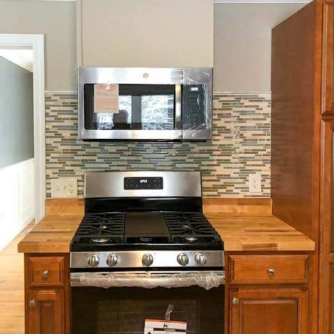 Kitchen stove with stainless steel microwave, wood cabinets, and mosaic tile backsplash