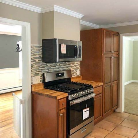 Kitchen with stainless stove and microwave, wood cabinets, tan tile floor, and doorway to adjacent rooms