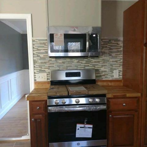 Compact kitchen with stainless steel stove and microwave, wood cabinets, and mosaic tile backsplash