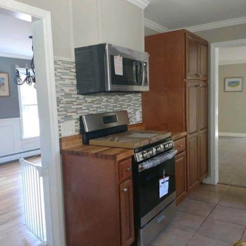 Kitchen with black appliances, wood cabinets, and beige tile flooring, viewed from a doorway