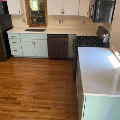 Compact kitchen with mint cabinets, wood floor, dark stove, dishwasher, and bright white island