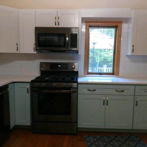 Small kitchen with white cabinets, black stove and microwave, and a window above the sink.
