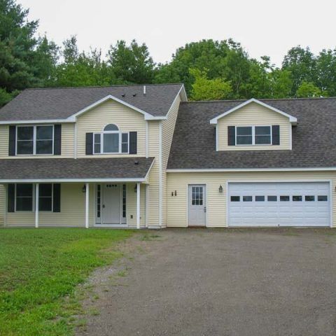 Suburban beige two-story house with attached garage, driveway, and green lawn
