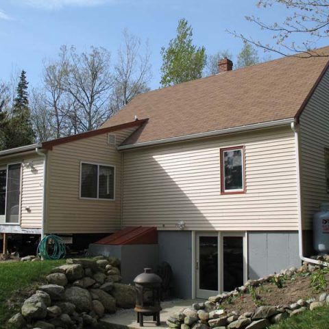 House exterior with tan siding, brown roof, and a stone garden in the foreground