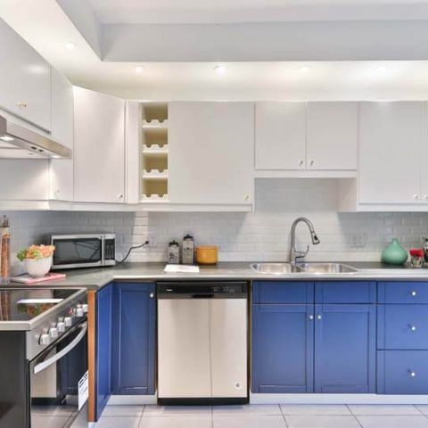 Modern kitchen with white upper cabinets, blue lower cabinets, stainless dishwasher, and white countertop