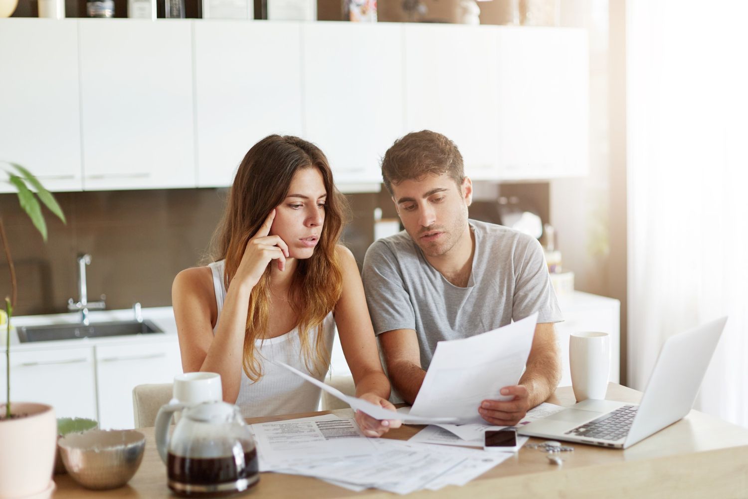 Two people reviewing papers at a kitchen table with a laptop and coffee pot nearby