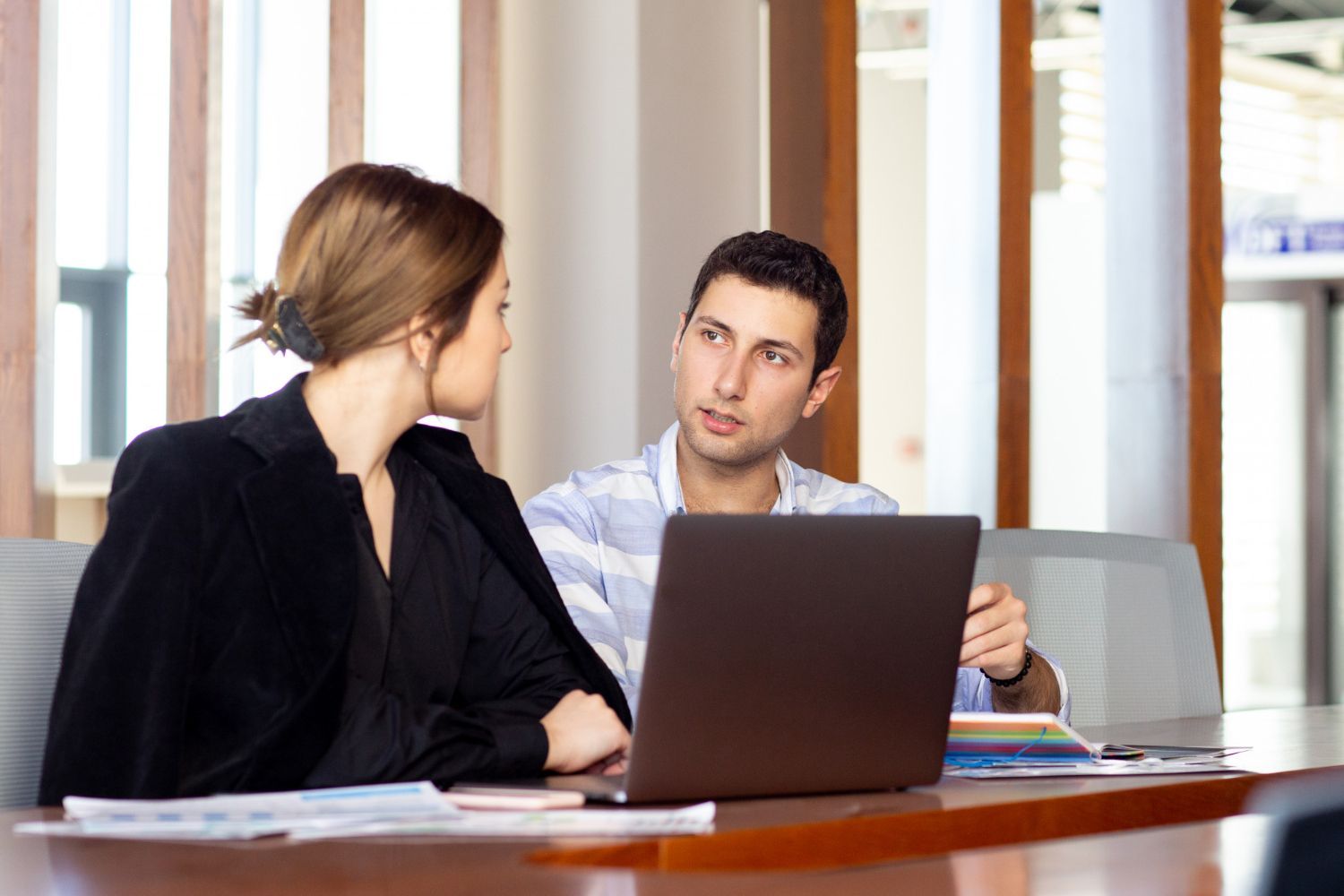 Two people talking at a table with a laptop in a bright office lounge