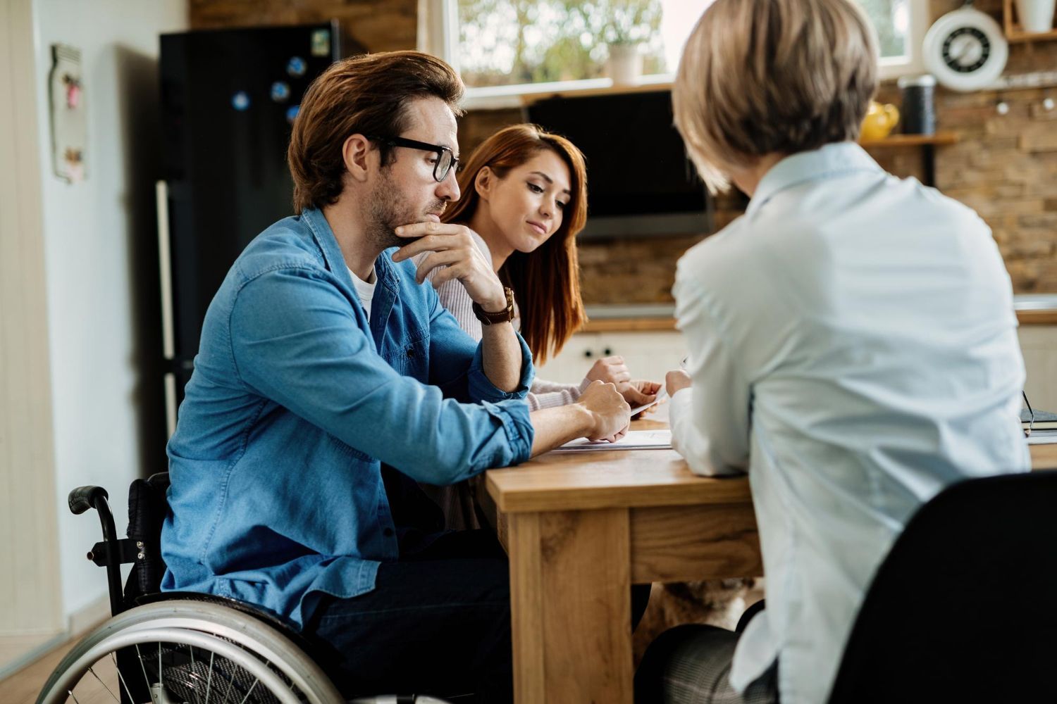 People seated at a kitchen table in conversation, with one person in a wheelchair in the foreground