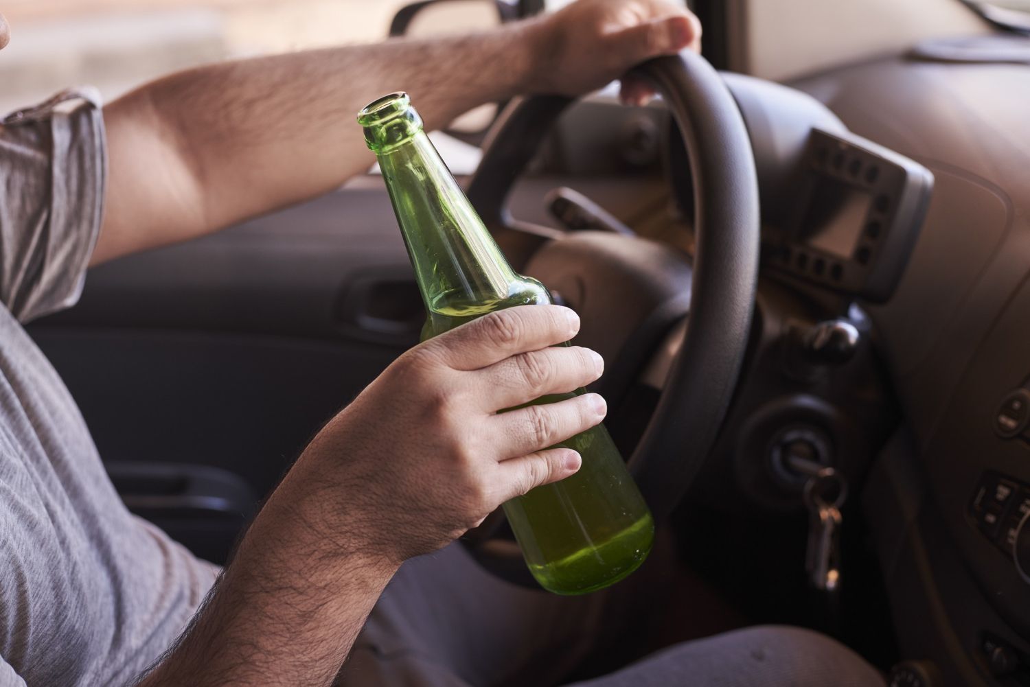 Driver holding a green bottle while steering a car