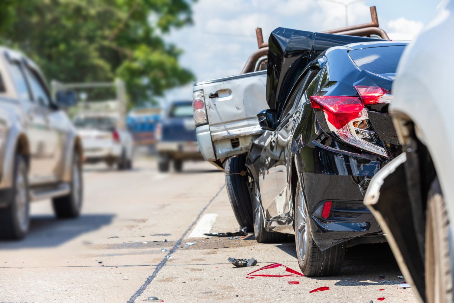 Damaged black sedan and white car in roadside collision, with debris on the pavement