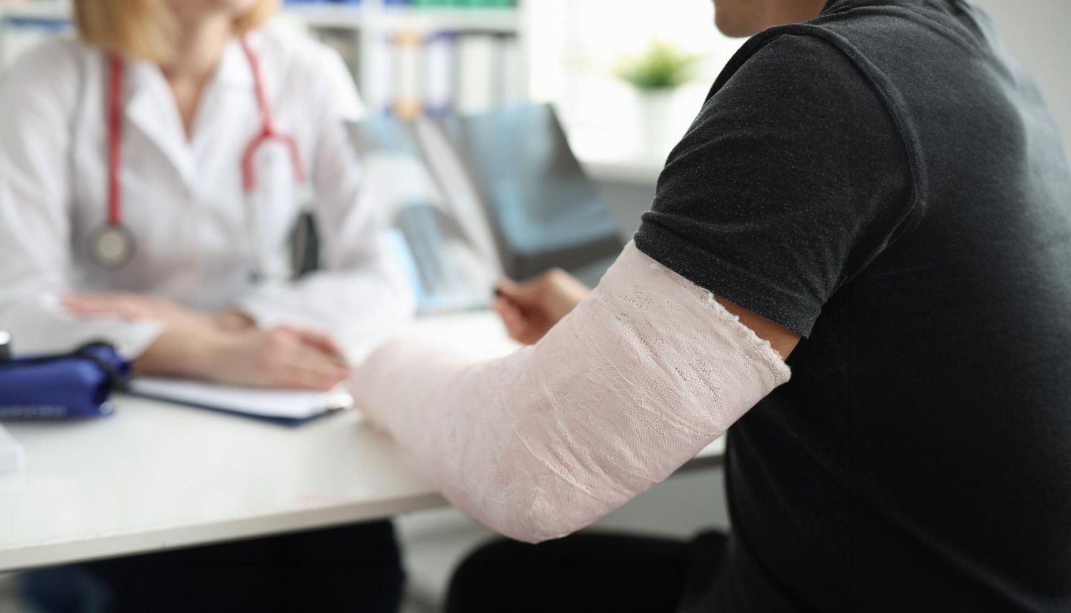 Patient with a bandaged arm speaking to a doctor in a clinic office